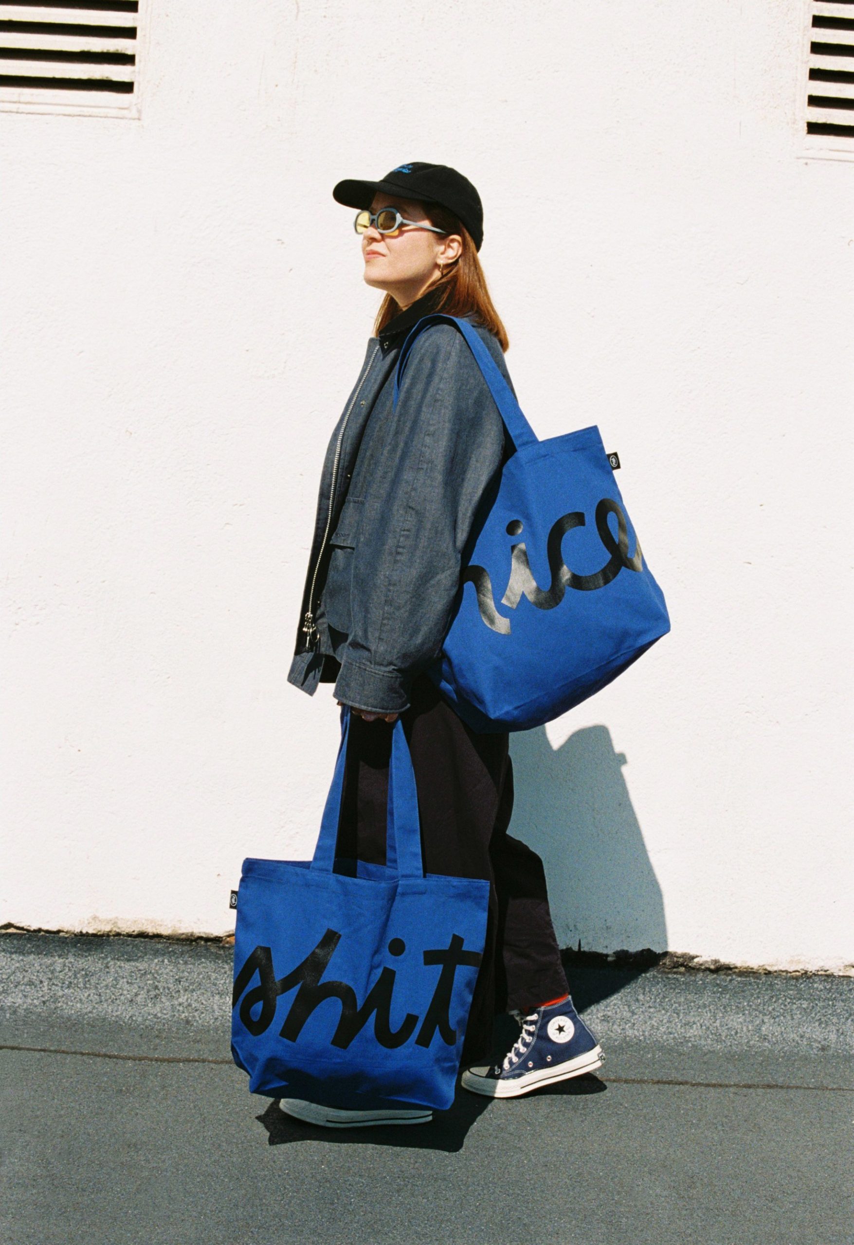 Image 5: A person carrying two blue Niceshit tote bags reading nice and shit.