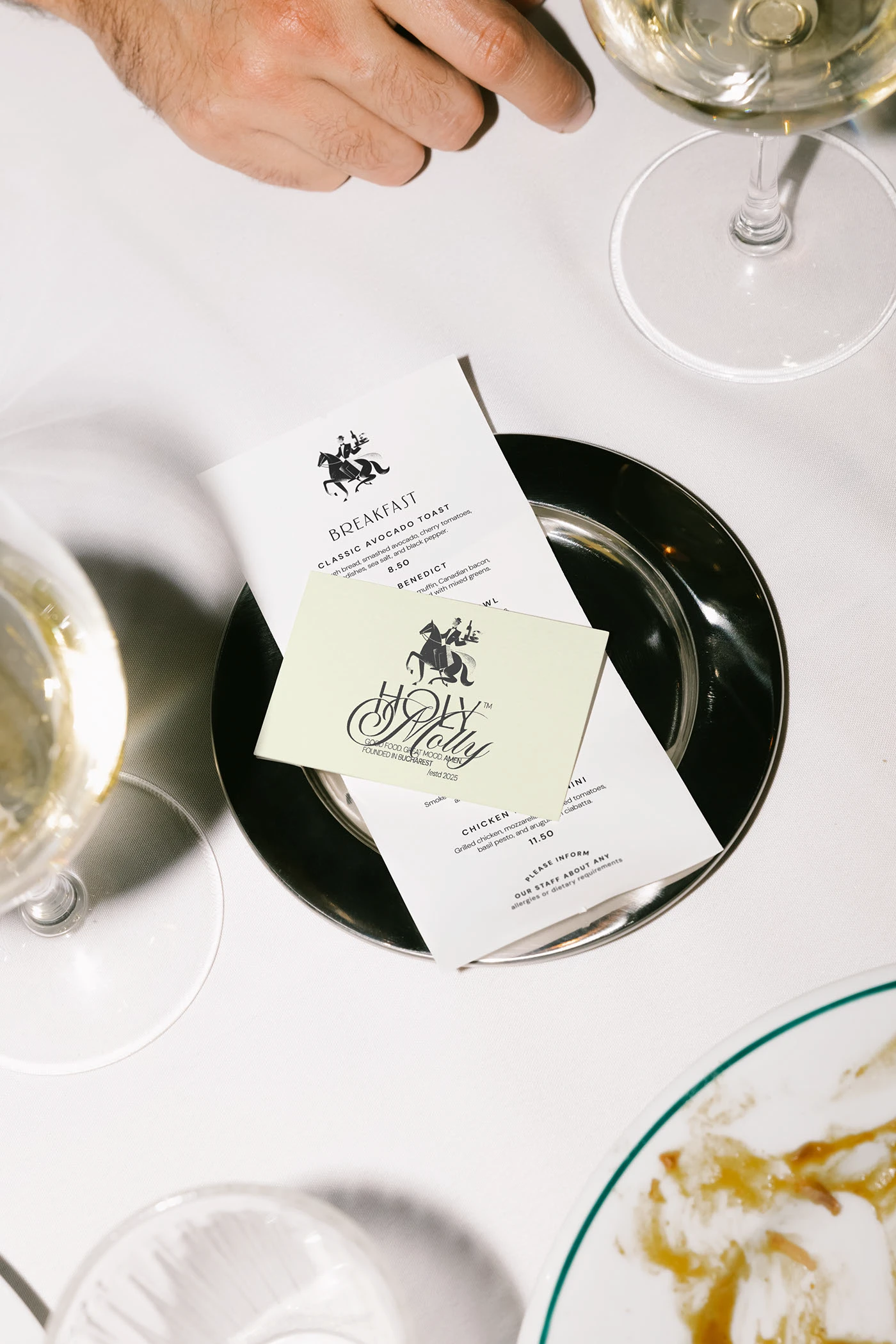 Image 4: Holy Molly menu card on cream stock laid on a black plate with wine glass — restaurant brand identity