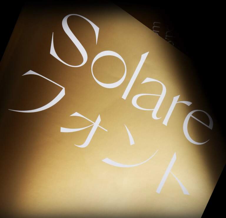 Image 1: sans serif typeface specimen on gold textured cylinder