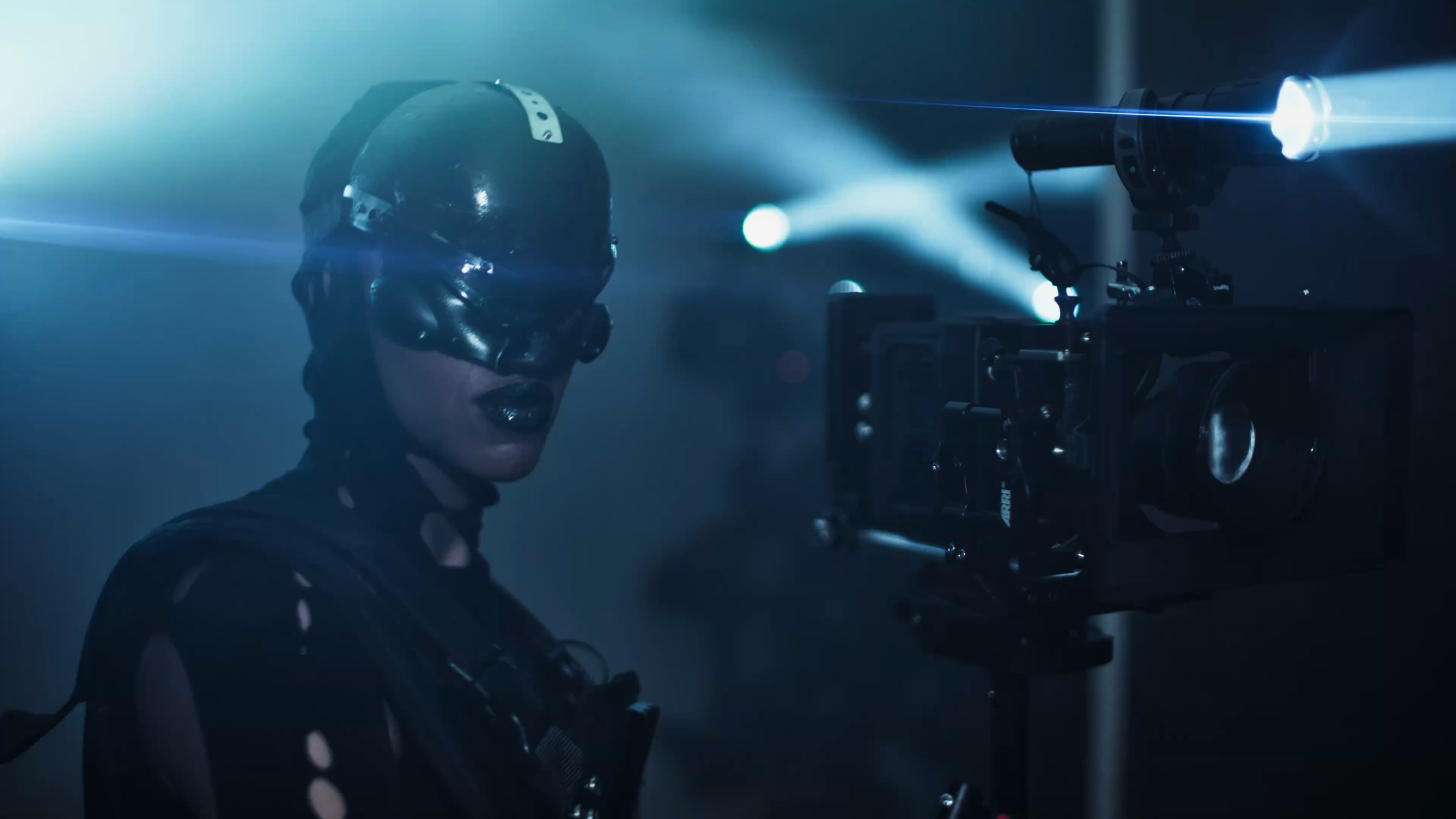 Image 2: A masked figure from the camera squad beside a cinema camera in Confessions II